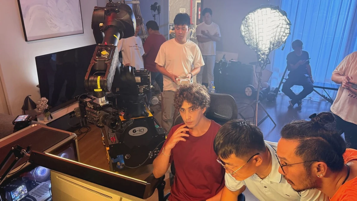近距离记录人体工学椅拍摄现场，机械臂搭载摄影机位于人物侧面，椅背、显示器和参与监看的团队同时入画