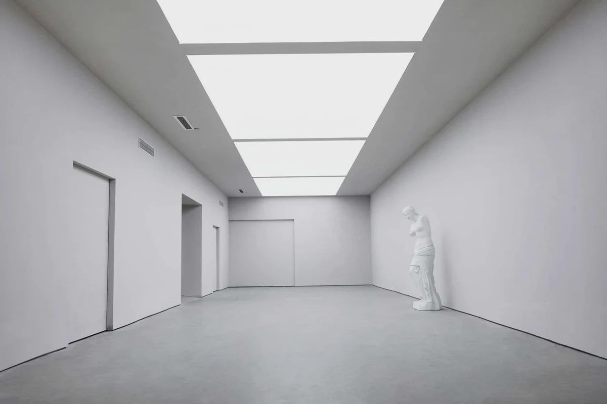White gallery with continuous ceiling light and a sculpture