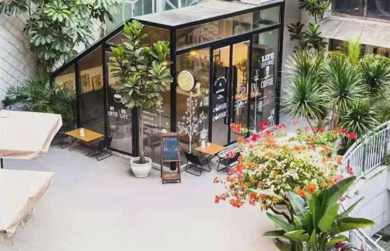 Glass café pavilion surrounded by dense planting and flowers