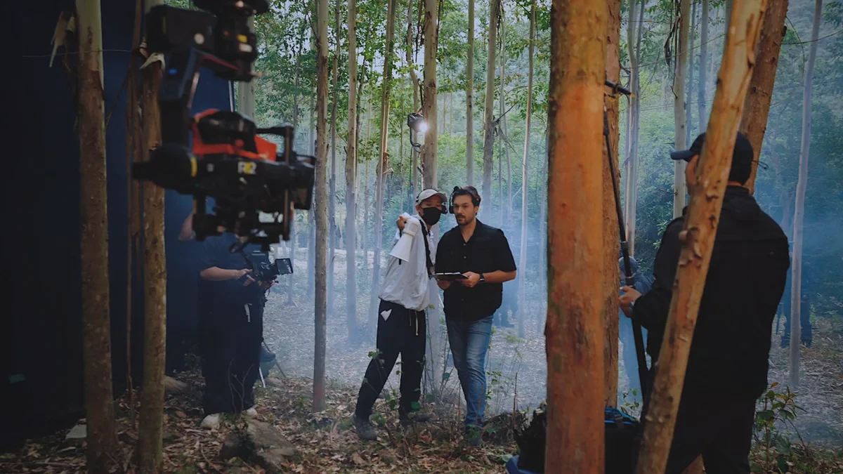 A production crew and camera equipment at an outdoor shoot among trees